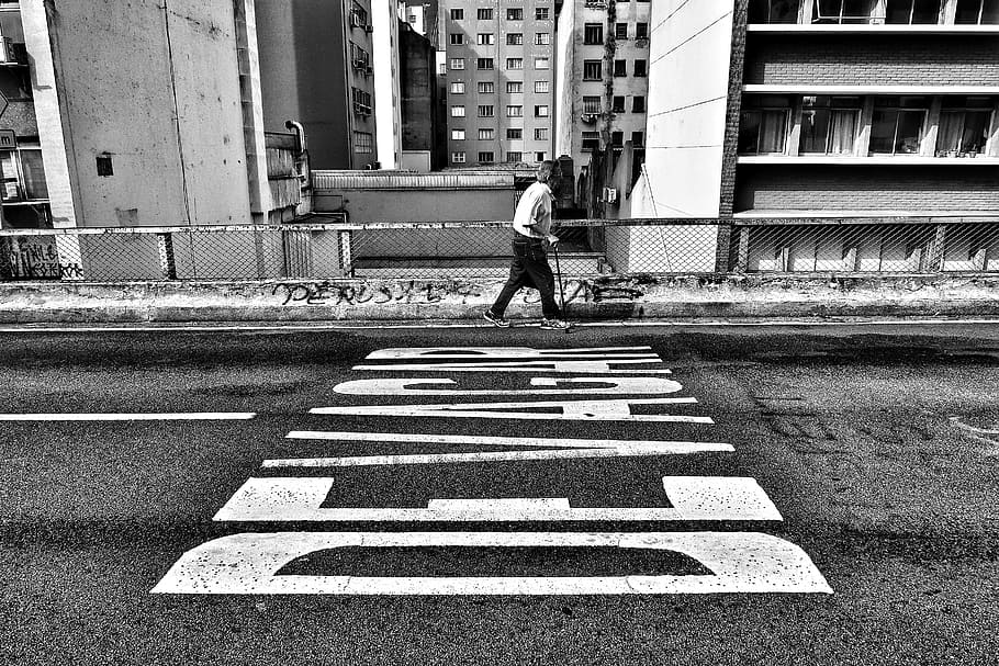 gray scale photography of person walking beside pave road, grayscale photography of man walking beside road