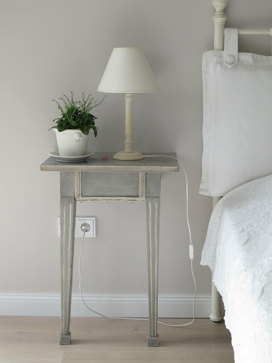 white table lamp near white pot on grey wooden end table, bedside