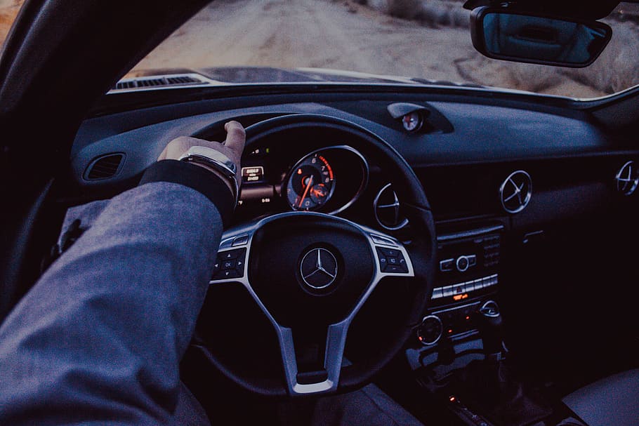 person driving Mercedes-Benz car, person holding black Mercedes-Benz steering wheel