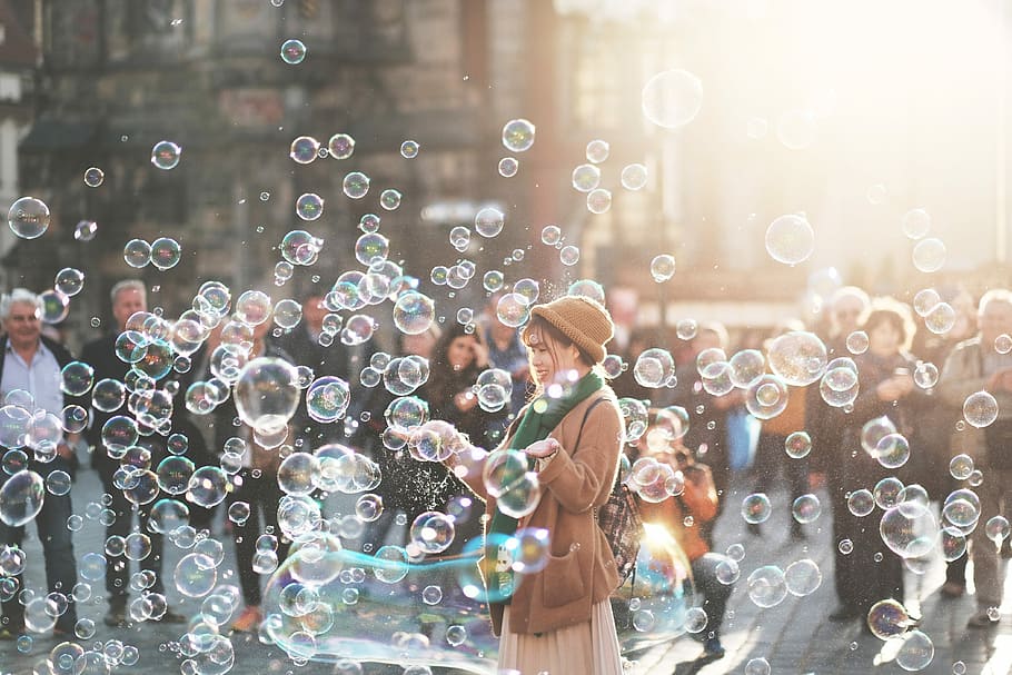 woman standing outdoor surrounded by bobbles during daytime, woman standing surrounded by bubbles during daytime