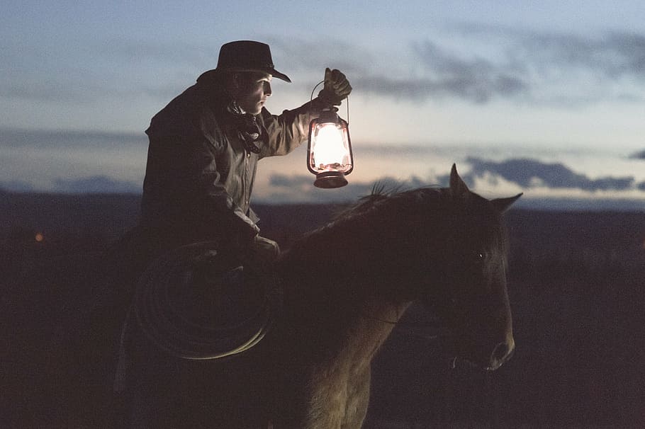 cowboy holding lantern riding on horse, lamp, sunset, guy, man, HD wallpaper