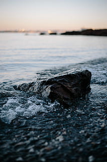 water hitting the rock on the coastline, closeup photo of black stone beside body of water HD wallpaper