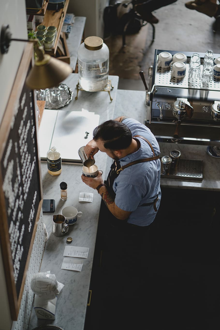man wearing blue shirt pouring coffee in his cup, high-angle photography of male barista