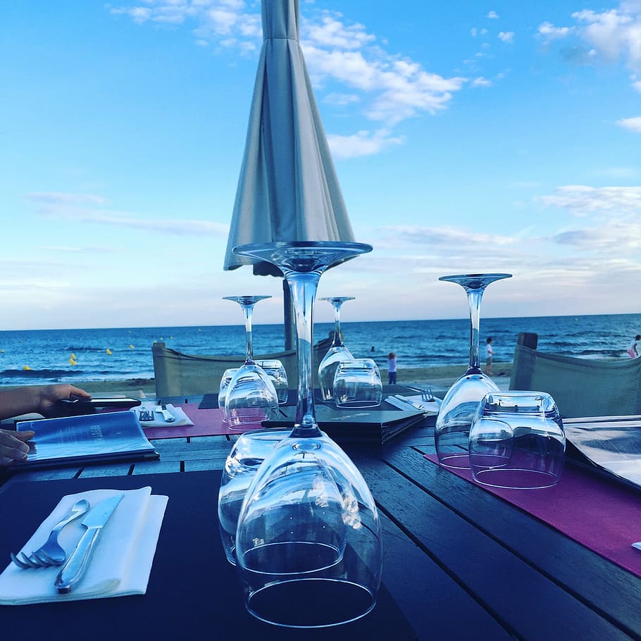 clear wine glasses near body of water, beach, restaurant, summer