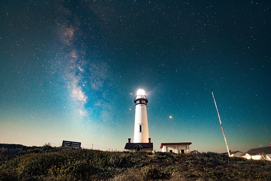 photo of turned on white lighthouse, white lighthouse between two houses on hill HD wallpaper