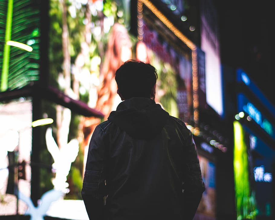 selective focus photography of person in leather jacket during nightime with LED signages background HD wallpaper