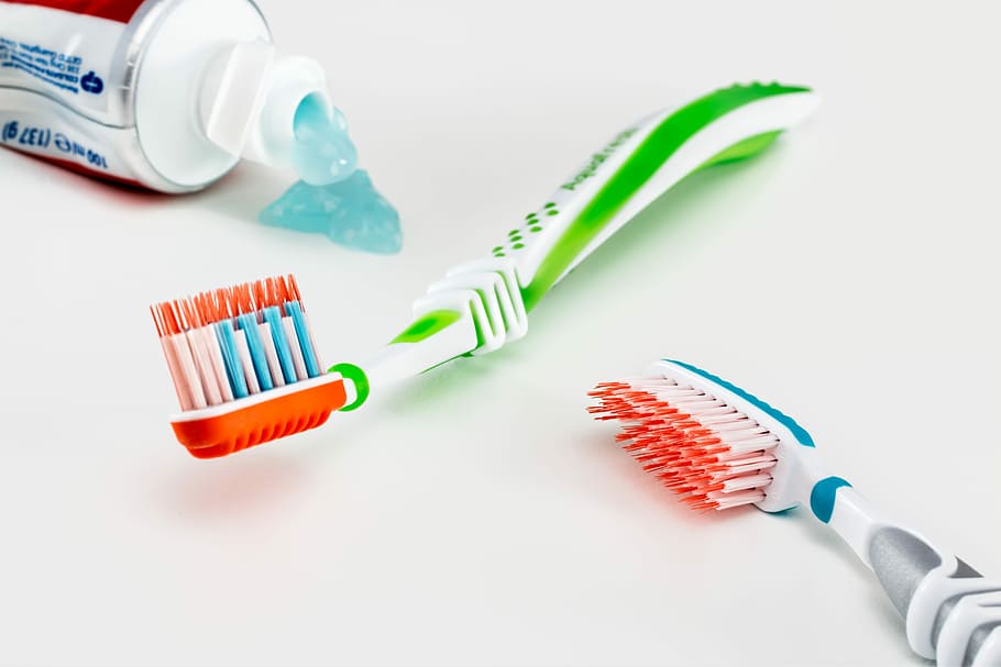 two green and gray toothbrushes on white surface, toothpaste