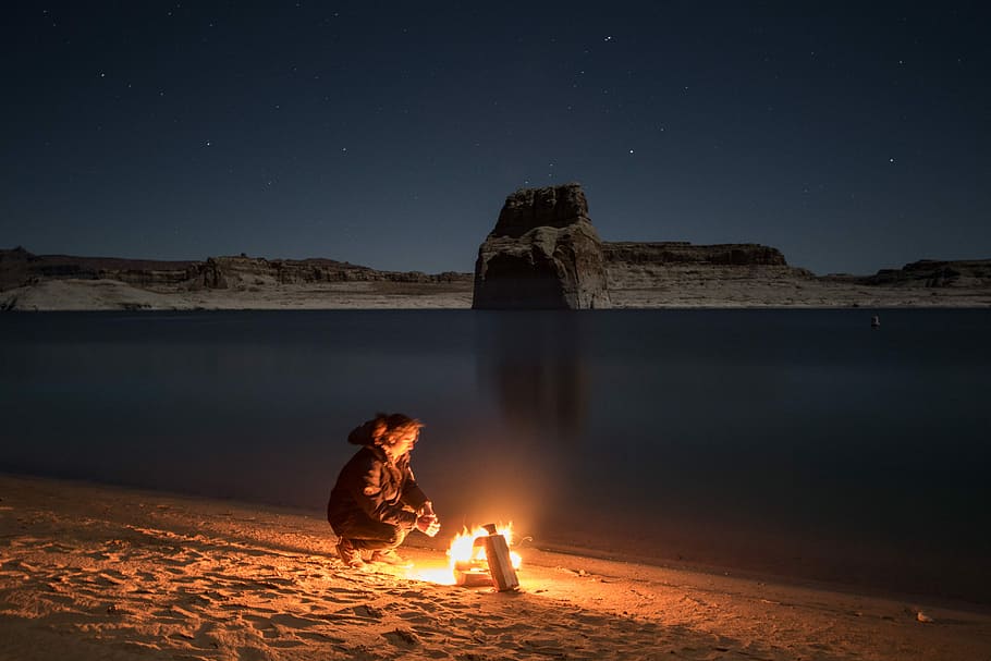 person sitting beside bonfire on seashore, woman sitting on sand facing bonfire beside seashore HD wallpaper