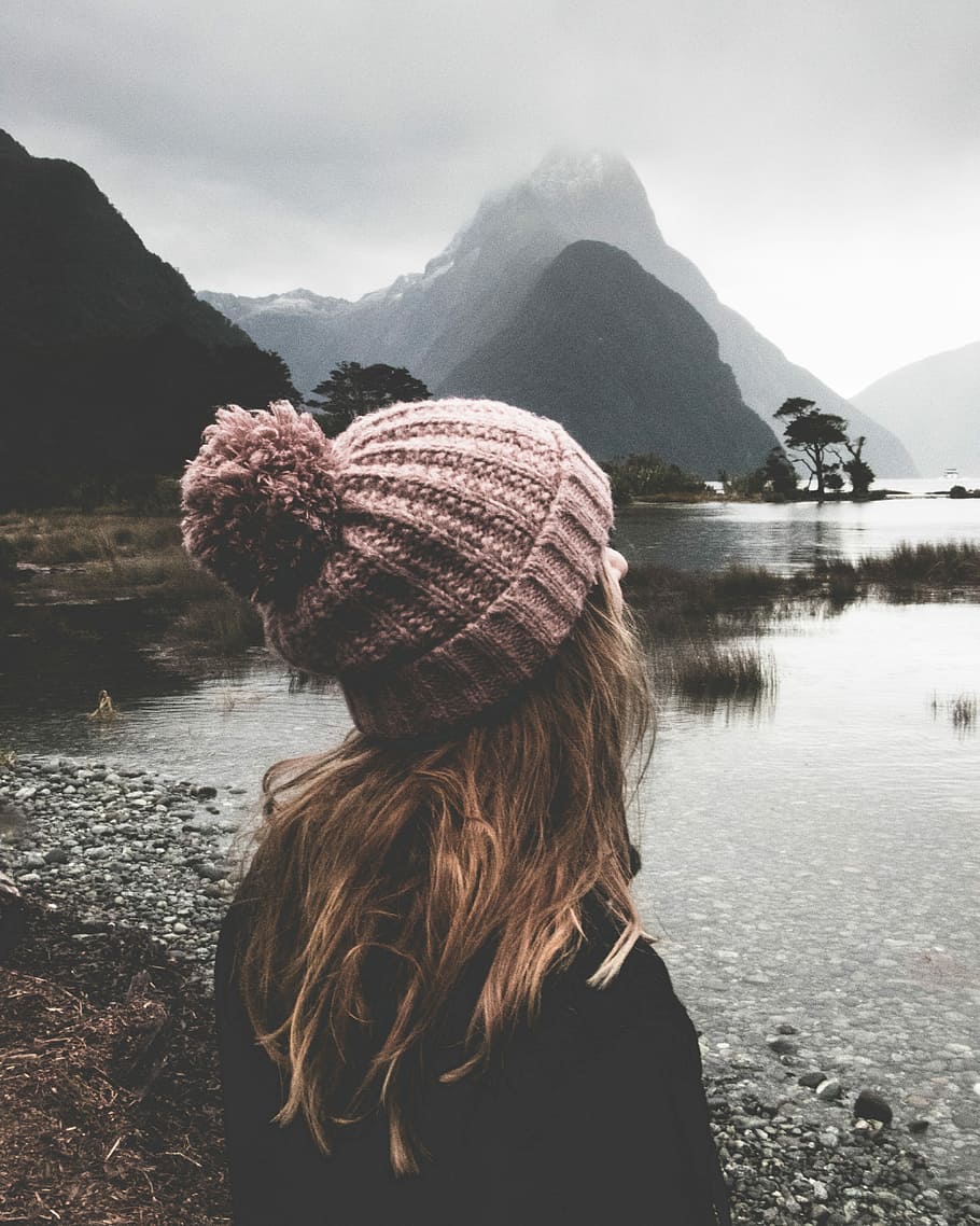 woman watching body of water during daytime, woman standing in front of calm body of water with mountain in distant under humid weather HD wallpaper