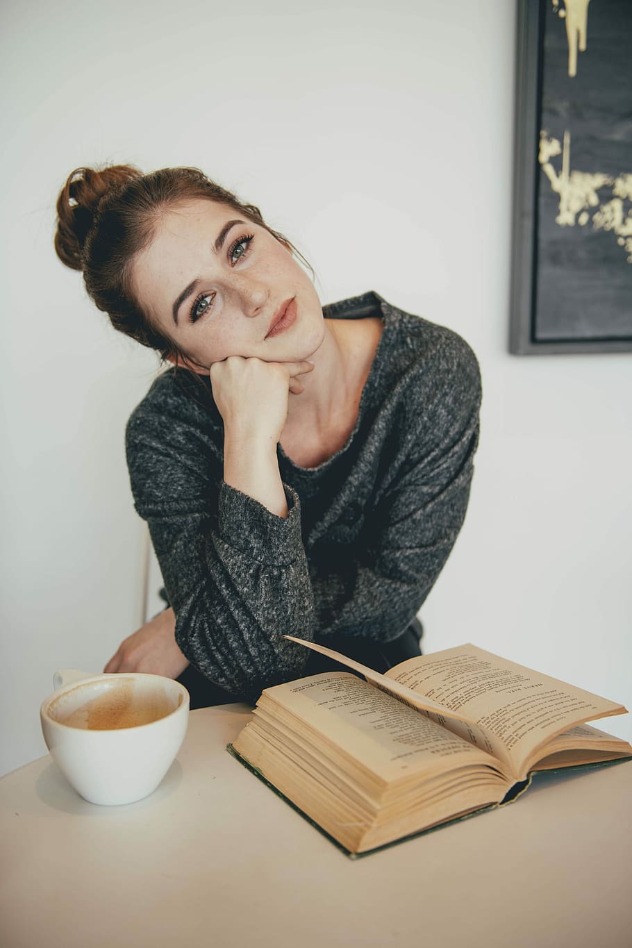 brown-haired woman in black sweater near brown book, woman sitting in front of white mug and opened book