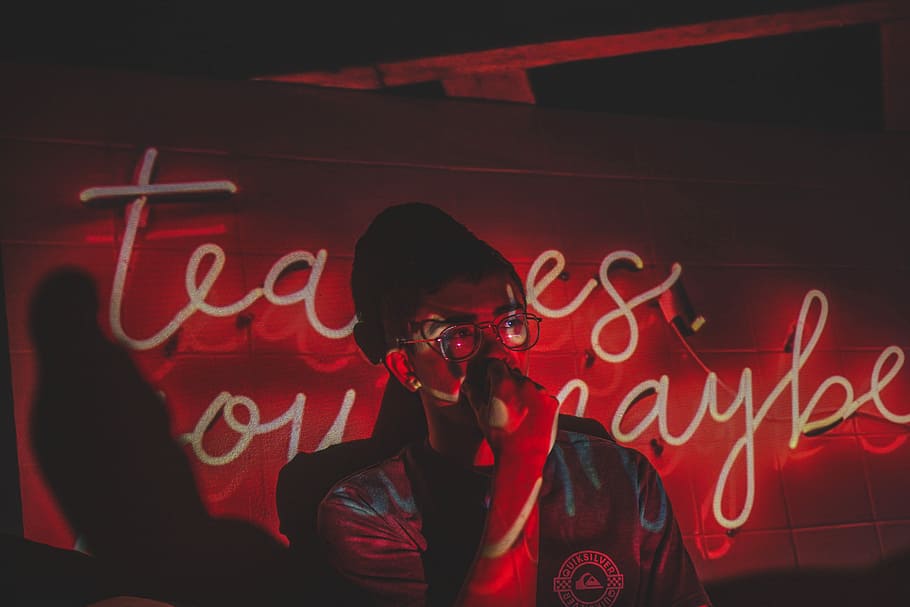 man standing in front of neon light signage in a dim lit room, person leaning on wall during nighttime HD wallpaper