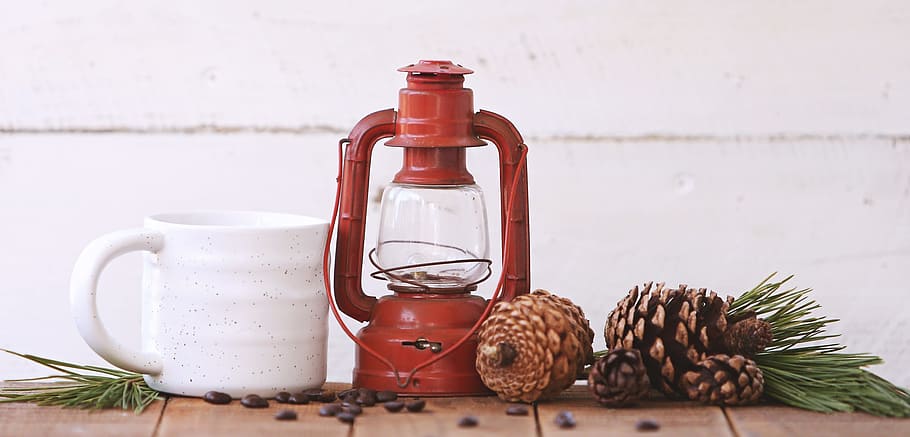 red kerosene lantern, white ceramic mug, and brown pine cones HD wallpaper