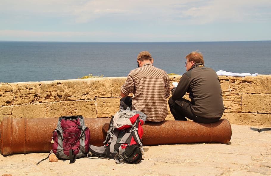 two man sitting in brown metal post near sea shore, hiking HD wallpaper