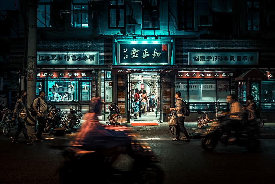 motorcycles and people passing by at night time, people walking near kanji script labeled building at nighttime