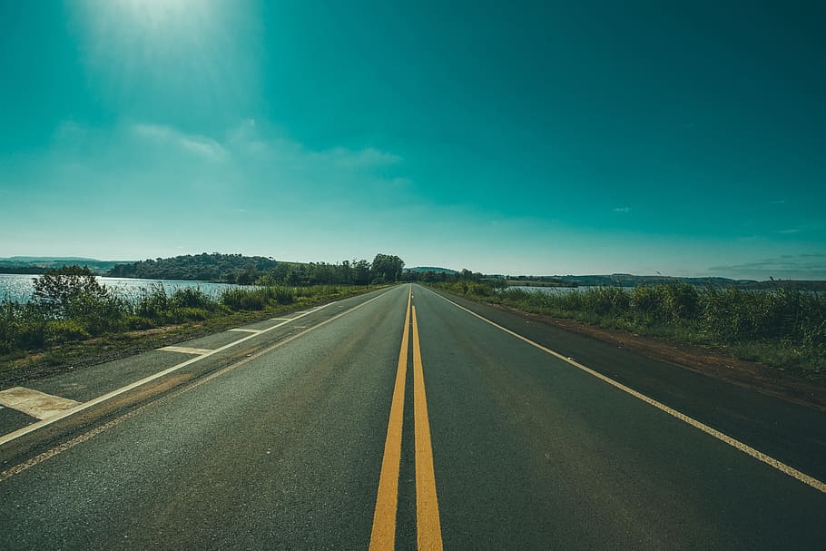 empty asphalt road under sun beside body of water, countryside