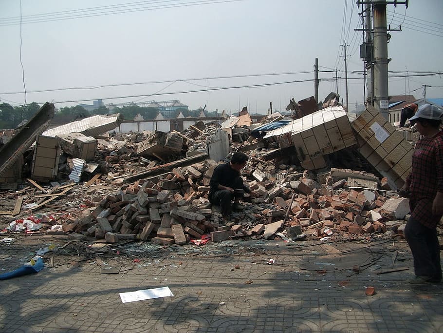 man sitting on concrete blocks of building debris during daytime