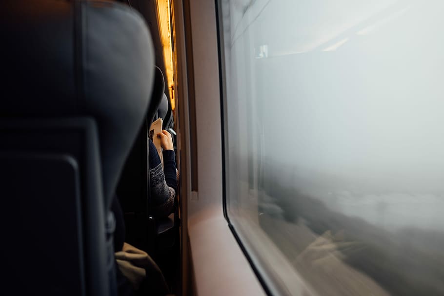 Person reading newspaper from behind with headrest in foreground near train carriage window, black bus chair HD wallpaper
