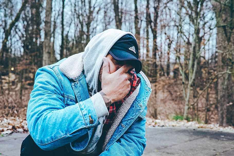 man in blue denim jacket covering his mouth with hand, man in blue denim jacket standing near tree during daytime, HD wallpaper
