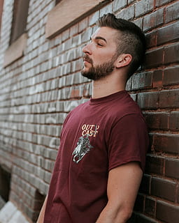 man leaning against brick wall, man wearing red crew-neck shirt HD wallpaper