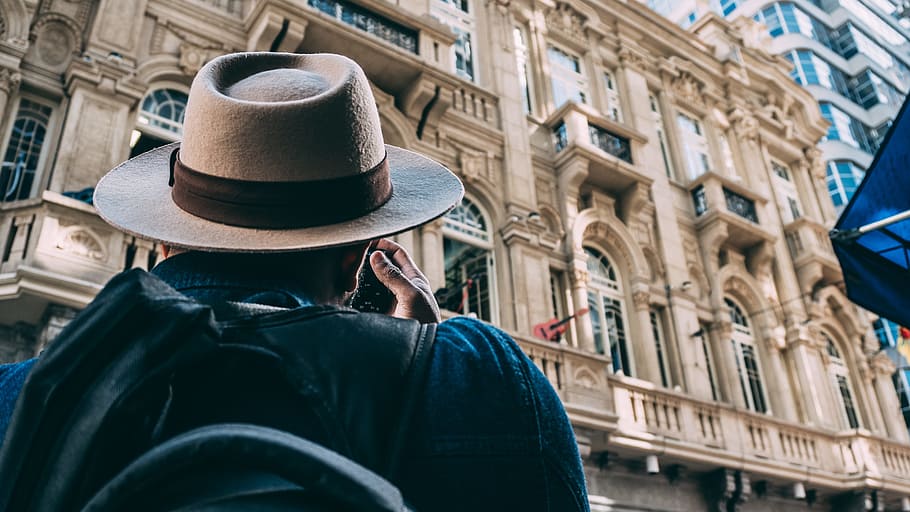 Man in Beige Hat Taking Picture on Beqige Conrete Architectural Building HD wallpaper