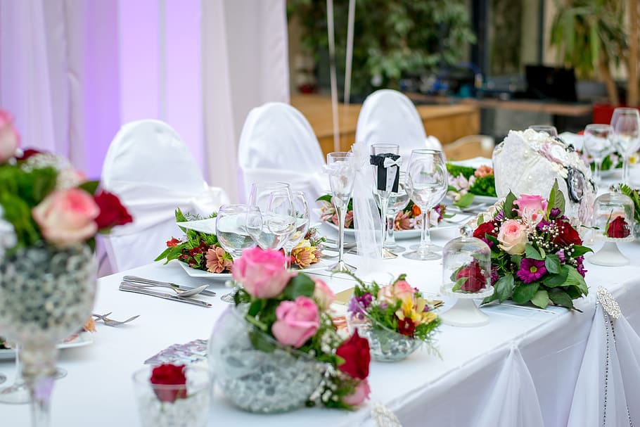 three flower arrangements on top of white table near drinking glasses and plates HD wallpaper