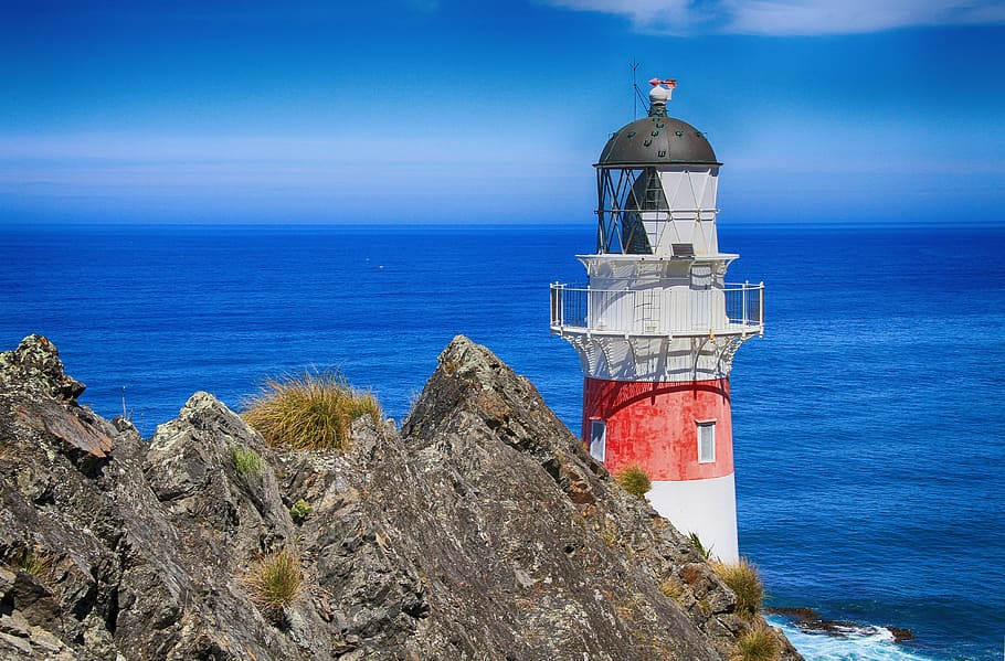 white and red lighthouse near grey rock formation and sea during daytime, HD wallpaper