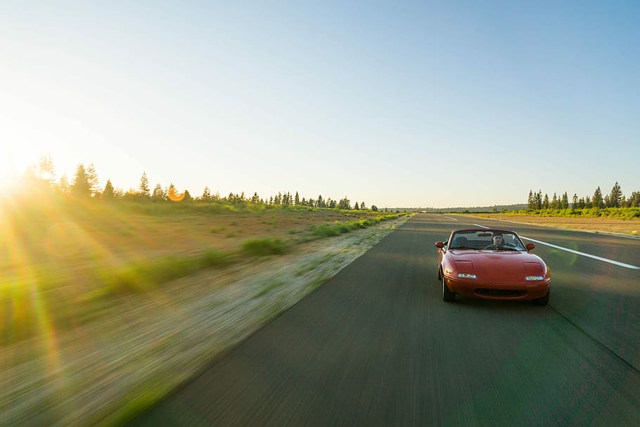 panning photography of red Mazda MX-5 Miata, red Mazda MX-5 convertible coupe on top of gray azphalted road under blue sky HD wallpaper