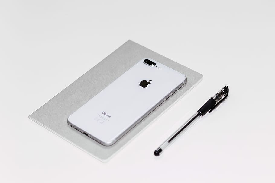 silver iPhone X beside black ballpoint pen, silver iPhone 8 Plus on notebook near pen