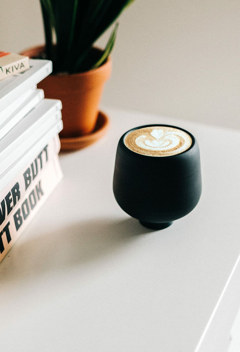 black ceramic teacup beside books and potted green plant on white wooden table, cup of espresso on white wooden table HD wallpaper
