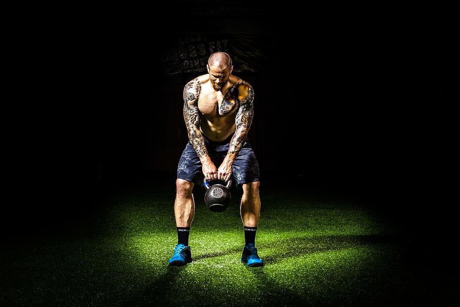 man with tattoos carrying black kettle bell, dark, effort, exercise