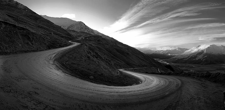 road surrounded by mountains, grayscale photography of empty dirt road near mountain