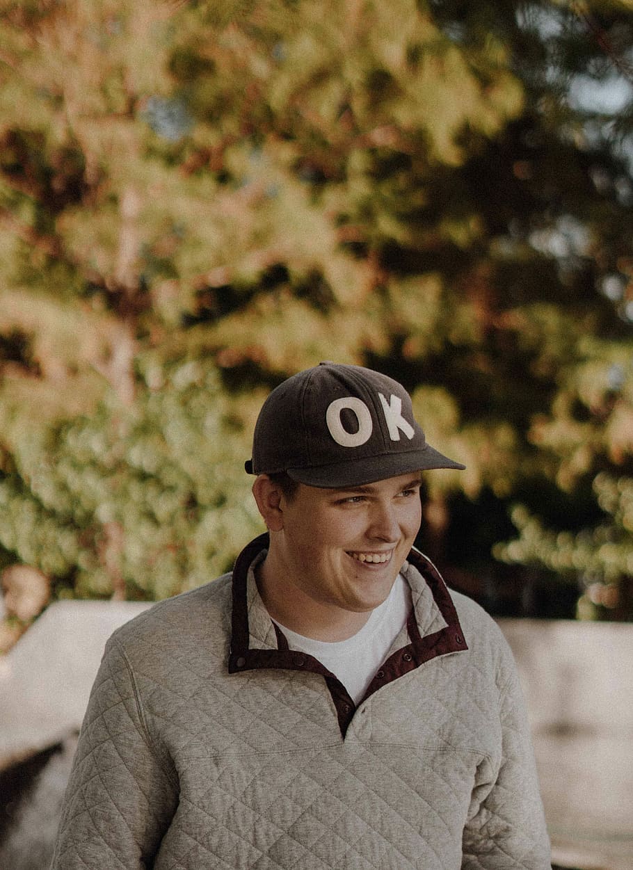 man in Ok cap and gilet, selective focus photography of man smiling HD wallpaper