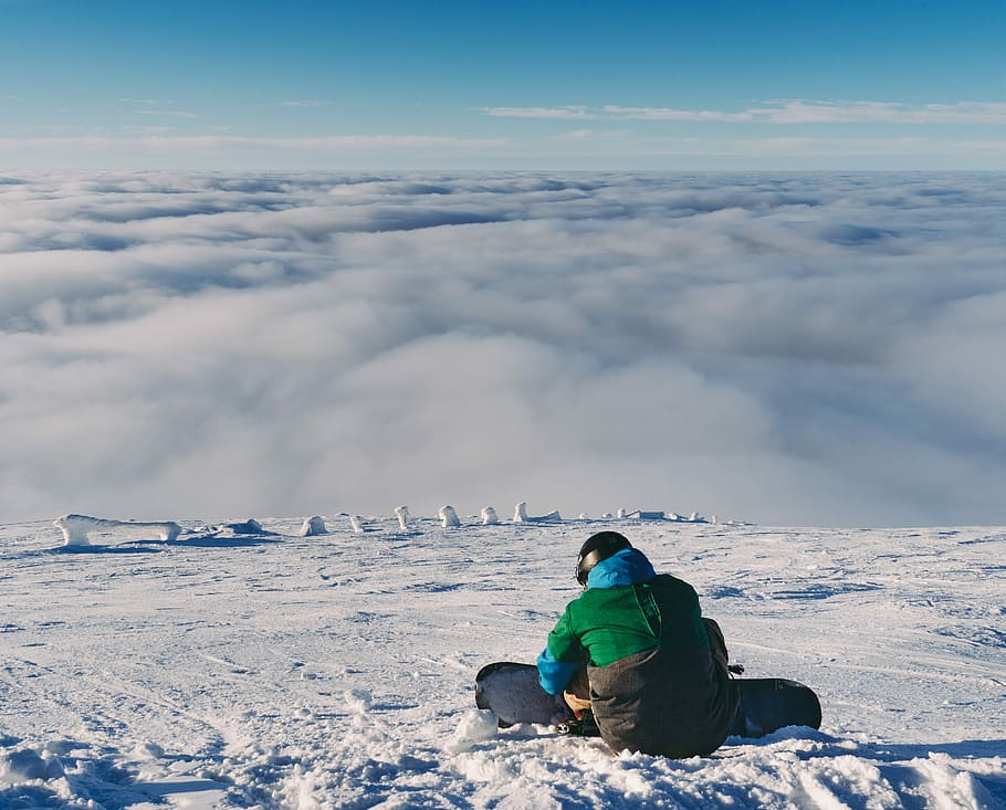 person holding snowboard while sitting on snow, man sitting on snow field during daytime HD wallpaper