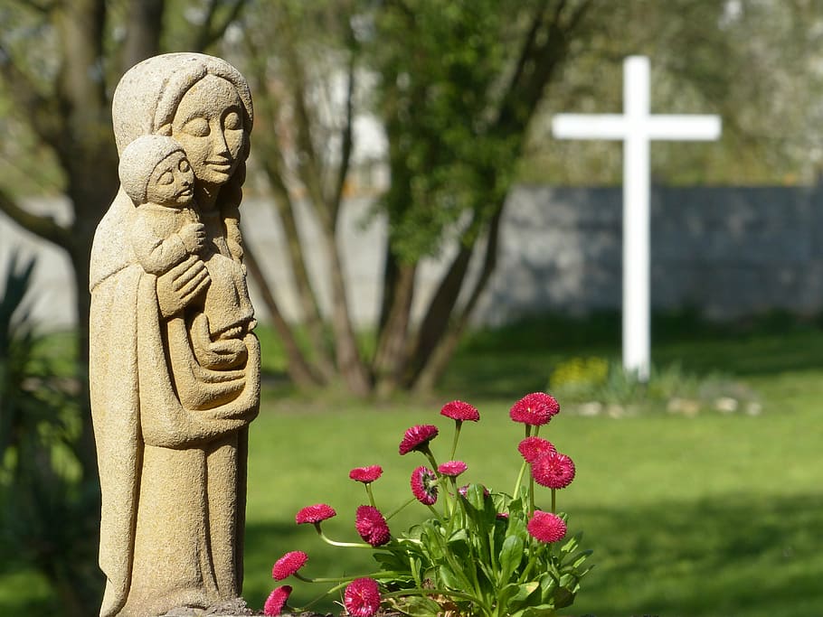 photo of mother and child statue standing beside red flowers
