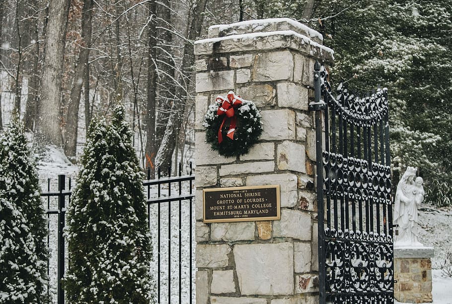 green wreath hanging on brown concrete wall, snow covered trees near white brick pole HD wallpaper
