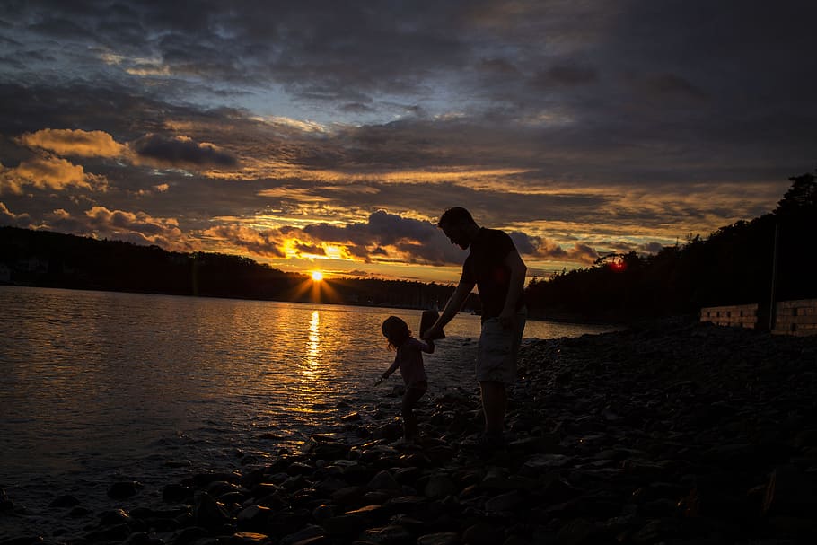 man holding the child on the body of water in golden hour photo