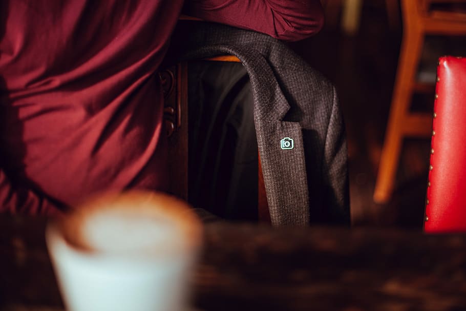 A blazer with an Unsplash pin, hanging on a chair at a cafe table, shallow focus photography of black coat HD wallpaper