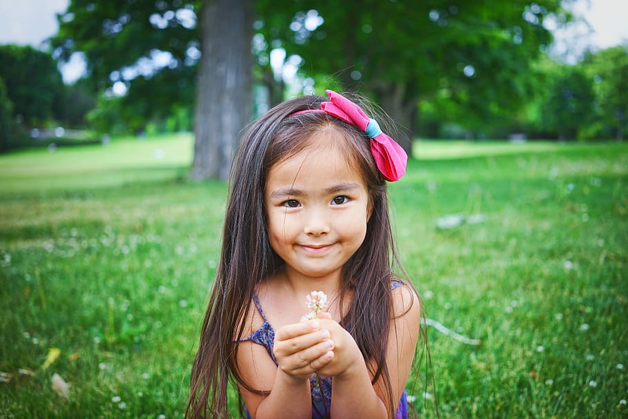 girl wearing black top while standing and holding flower on green grass, girl holding white flower while smiling HD wallpaper