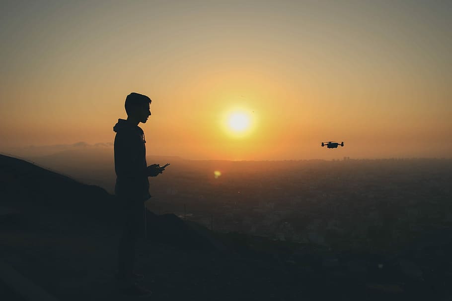 Sunset flights, silhouette of person flying drone on mountain in distant of buildings HD wallpaper