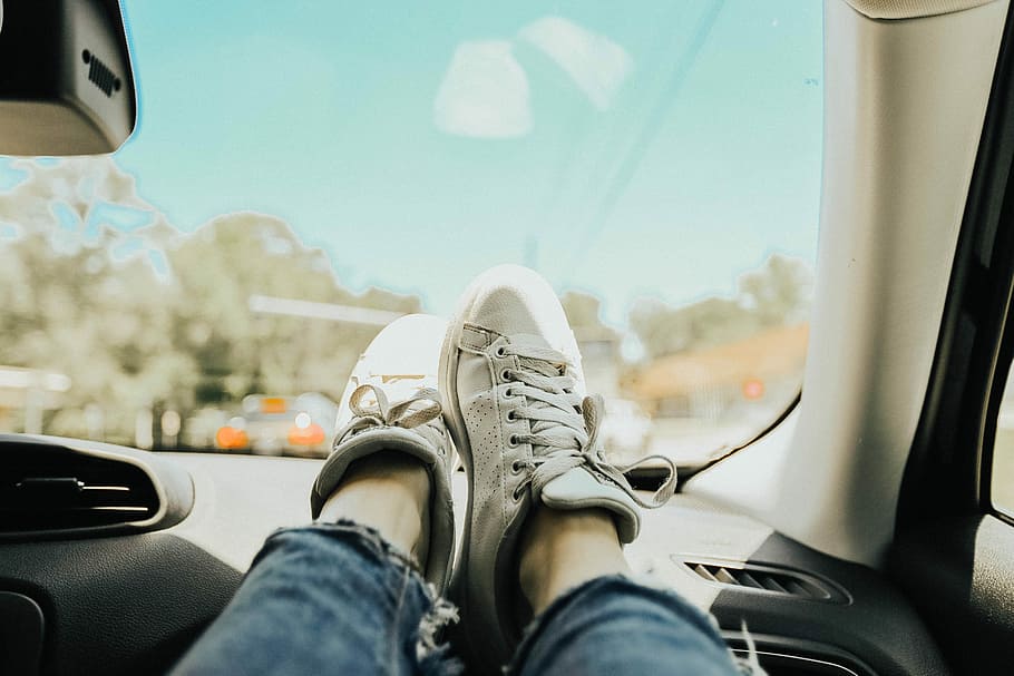 person resting feet on car dashboard, person wearing white shoes on top of black vehicle dashboard