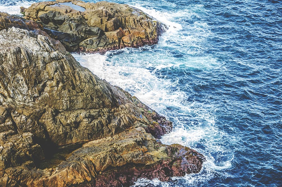 aerial photo of sea waves splashing through rocky mountain, aerial view of green and gray mountain near body of water HD wallpaper