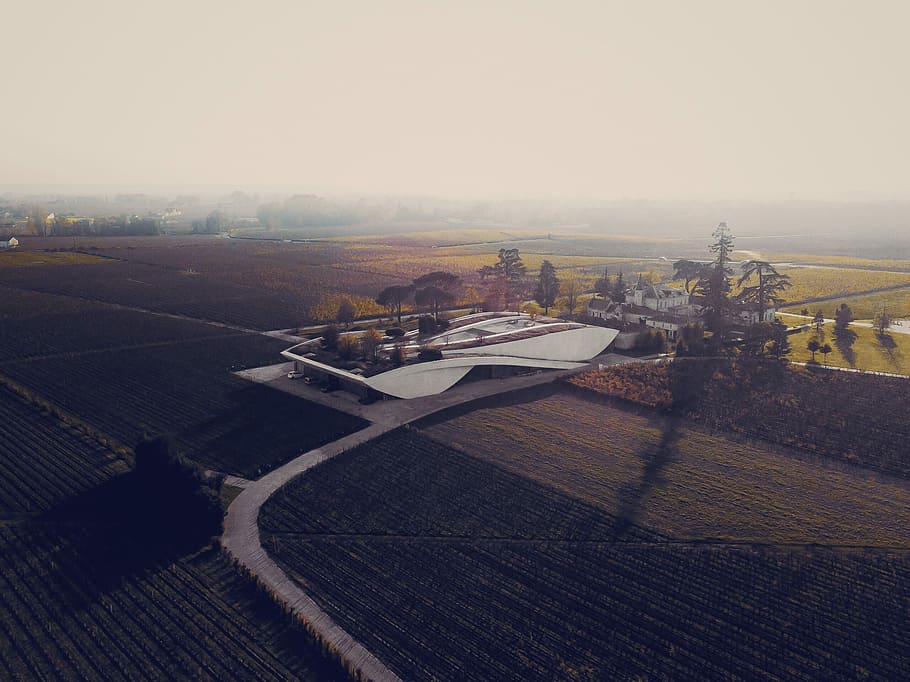 gray concrete building surrounded with green fields during cloudy day, white concrete building in the middle of farmland at daytime HD wallpaper