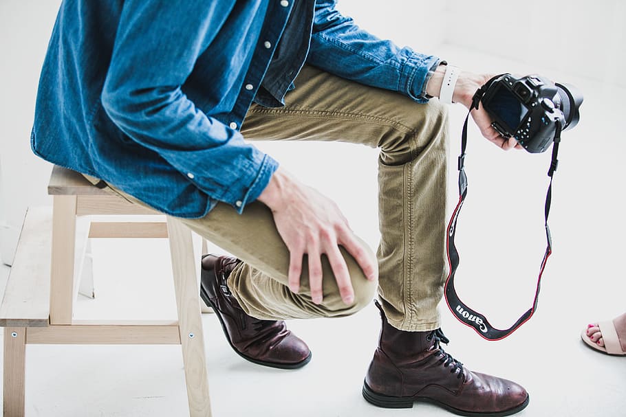 man holding DSLR camera while sitting on stool, person holding camera while sitting HD wallpaper
