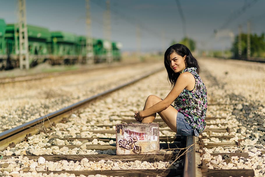 woman wearing black and multicolored sleeveless top and blue denim shorts outfit sitting on train railways under blue sky during daytime, HD wallpaper