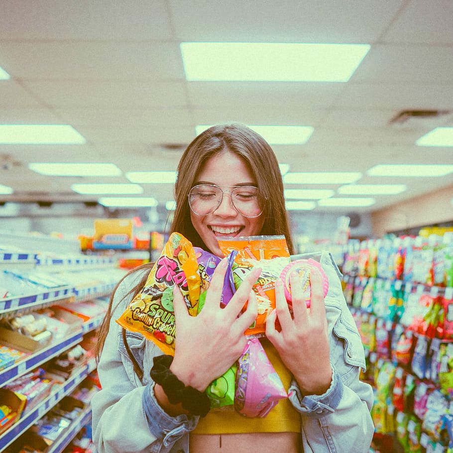 smiling woman holding pack of food inside grocery store, woman holding gummies pack while smiling, HD wallpaper