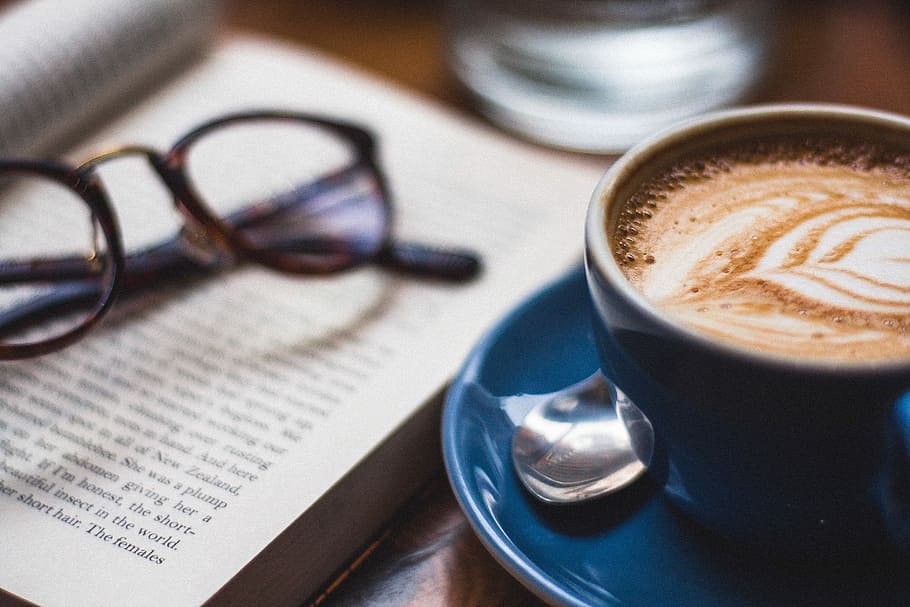 black framed eyeglasses on book beside cappuccino, latte coffee beside sunglasses