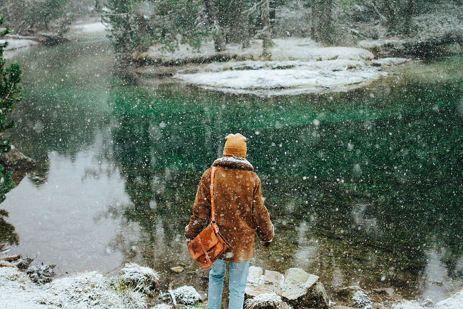 person wearing jacket standing near body of water, person facing body of water under falling snow HD wallpaper