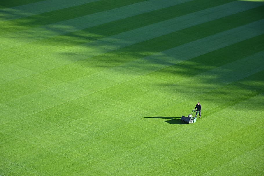 aerial photography of person trimming sports field during day, man pushing lawn in the middle of field HD wallpaper