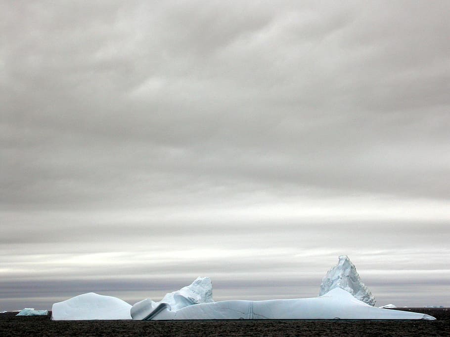ice berg surrounded by body of water under dark cloudy sky, landscape photo of ice island