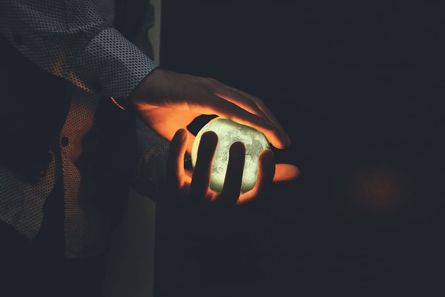 Closeup shot of a man’s hands holding a glowing orb, people